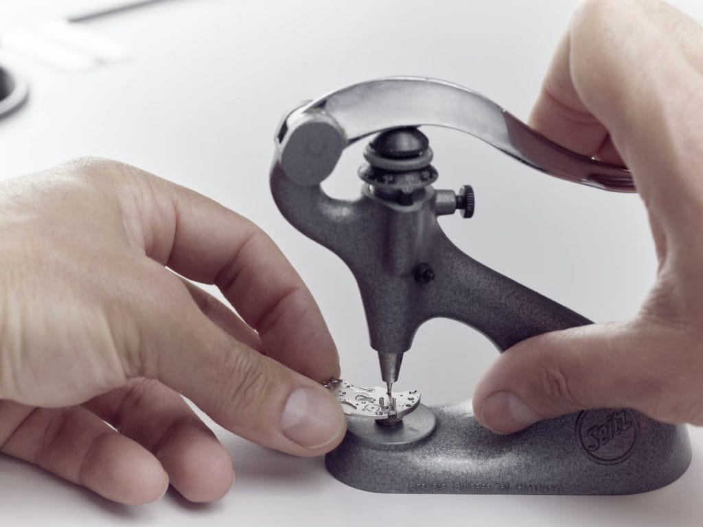 Lorsque cela est possible, les composants usés sont restaurés ou reproduits à l'identique avec des techniques et matériaux d'époque. Ici, l'horloger déchasse une pierre abîmée du pont de barillet.