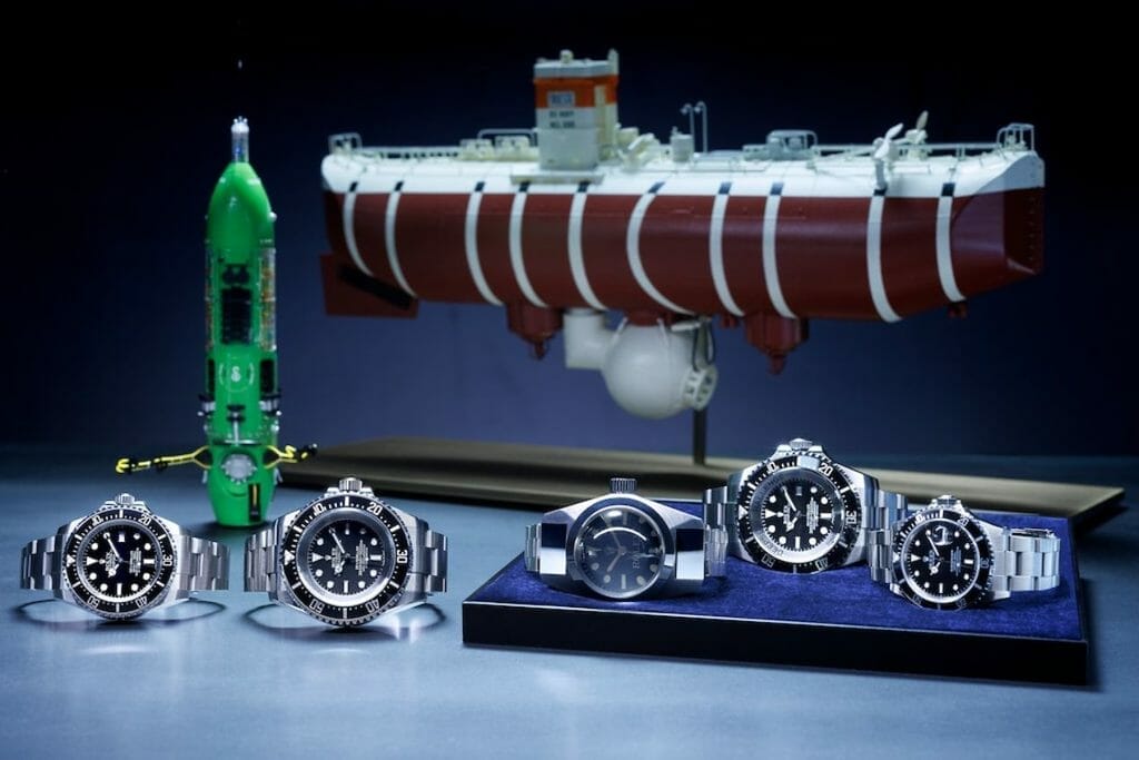 Premier plan, de gauche à droite : Oyster Perpetual Rolex Deepsea (2008), Oyster Perpetual Deepsea Challenge (2022), Deep Sea Special (1960), Rolex Deepsea Challenge (2012) et Oyster Perpetual Submariner (1986). Arrière-plan de gauche à droite : maquettes du submersible DEEPSEA CHALLENGER et du bathyscaphe Trieste.